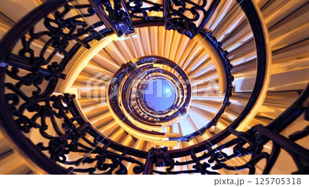 Multiple perspectives of an elegant spiral staircase winding upwards, its dark wooden handrail contrasting with cream colored steps, leading eye towards gently illuminated ceiling Multiple perspectives of an elegant spiral staircase winding upwards, its dark wooden handrail contrasting with cream colored steps, leading eye towards gently illuminated ceiling 125705318