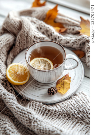 A cozy scene featuring a cup of tea with a lemon slice, surrounded by a knitted blanket and autumn leaves. 125705471