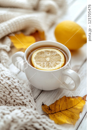 A cozy scene featuring a cup of tea with a lemon slice, surrounded by a knitted blanket and autumn leaves. 125705476