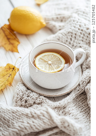 A cozy scene featuring a cup of tea with a lemon slice, surrounded by a knitted blanket and autumn leaves. 125705482