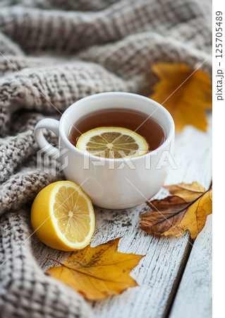A cozy scene featuring a cup of tea with a lemon slice, surrounded by a knitted blanket and autumn leaves. A cozy scene featuring a cup of tea with a lemon slice, surrounded by a knitted blanket and autumn leaves. 125705489