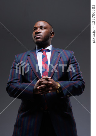 Confident businessman in a stylish striped suit and tie, posing with hands clasped. Professional portrait, leadership, success, corporate style, authority, and ambition concept. Dark background. Confident businessman in a stylish striped suit and tie, posing with hands clasped. Professional portrait, leadership, success, corporate style, authority, and ambition concept. Dark background. 125706383