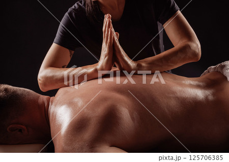 Close-up of therapist pressing palms together on man's back during deep tissue massage therapy for muscle relief. 125706385