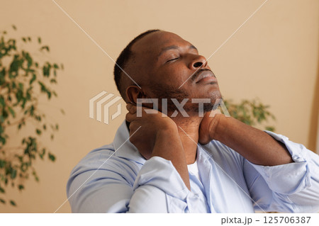 Close-up of a man experiencing neck pain, holding the back of his neck with both hands, eyes closed in discomfort. Concept of muscle strain, tension, or cervical spine issues. Health problem. 125706387