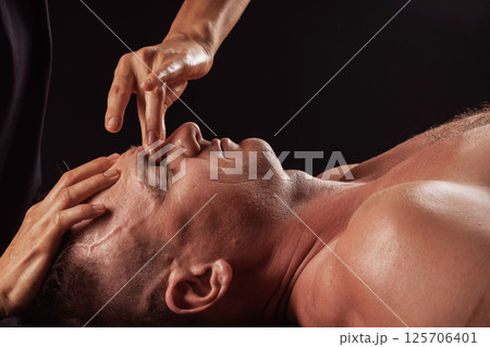 Close-up of male face during professional facial massage therapy, therapist applying pressure to brow area. Close-up of male face during professional facial massage therapy, therapist applying pressure to brow area. 125706401