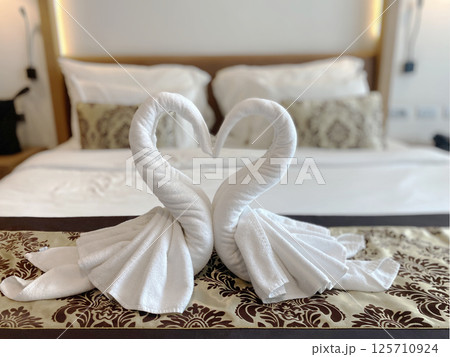 Romantic swan towel art arranged in a heart shape on a bed in a luxury hotel room, symbolizing love and hospitality blurred background. Romantic swan towel art arranged in a heart shape on a bed in a luxury hotel room, symbolizing love and hospitality blurred background. 125710924