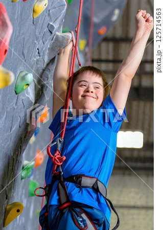 Climber With Down Syndrome Enjoys Indoor Rock Climbing at a Sports Facility in Bright Blue Gear Climber With Down Syndrome Enjoys Indoor Rock Climbing at a Sports Facility in Bright Blue Gear 125714563