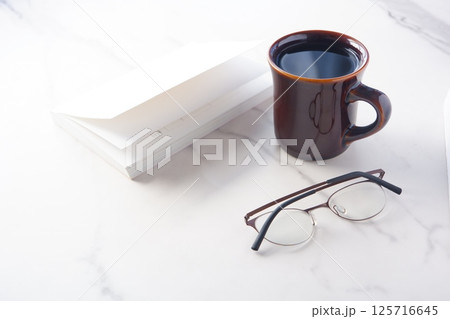 白いテーブルの上の一冊の本とメガネ、コーヒーのマグカップで、コーヒーを飲みながら読書を楽しむイメージ 125716645