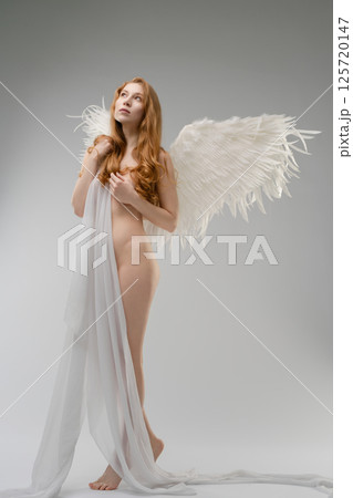 Naked woman with wings and body art poses in minimalistic studio Naked woman with wings and body art poses in minimalistic studio 125720147