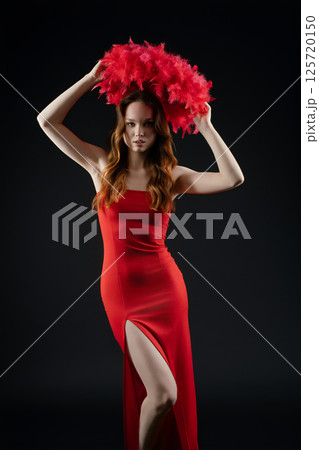 Woman posing with dramatic red feathered headpiece in a studio setting, showcasing emotion and style Woman posing with dramatic red feathered headpiece in a studio setting, showcasing emotion and style 125720150