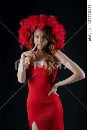 Woman expresses emotions while posing in a striking red dress and feathered headpiece in a studio setting Woman expresses emotions while posing in a striking red dress and feathered headpiece in a studio setting 125720151