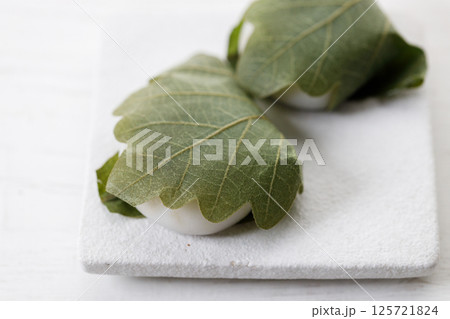 Closeup of Kashiwa mochi. Traditional Japanese sweet from white mochi or rice cake and sweet Anko or red bean paste filling surrounded with Kashiwa or Oak leaf . Closeup of Kashiwa mochi. Traditional Japanese sweet from white mochi or rice cake and sweet Anko or red bean paste filling surrounded with Kashiwa or Oak leaf . 125721824