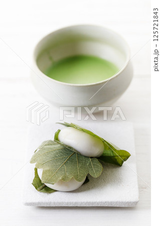 Kashiwa mochi and Cup of fresh matcha tea. Japanese sweet from mochi or rice cake and sweet red bean paste filling surrounded with Kashiwa or Oak leaf . Kashiwa mochi and Cup of fresh matcha tea. Japanese sweet from mochi or rice cake and sweet red bean paste filling surrounded with Kashiwa or Oak leaf . 125721843