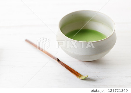 Cup of fresh matcha tea, green tea and Chashaku or tea scoop, equipments for preparing matcha green tea, on white wooden table. Cup of fresh matcha tea, green tea and Chashaku or tea scoop, equipments for preparing matcha green tea, on white wooden table. 125721849