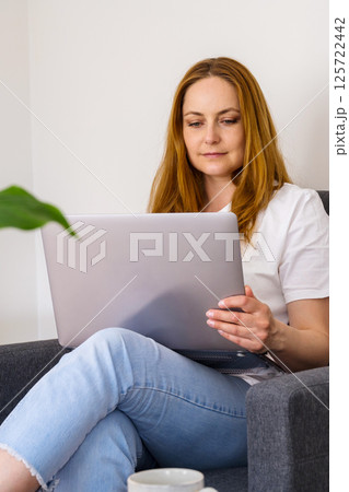 Woman working online, sitting in armchair and using laptop  125722442