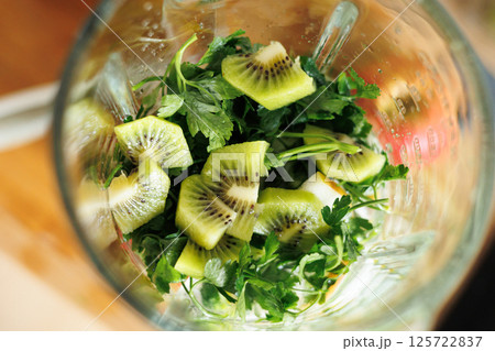 Close up view of kiwi and parsley inside of glass blender bowl on table top at modern home kitchen. Healthy ingredients, Fruits and greens, for detox smoothie drink and lifestyle diet. Close up view of kiwi and parsley inside of glass blender bowl on table top at modern home kitchen. Healthy ingredients, Fruits and greens, for detox smoothie drink and lifestyle diet. 125722837