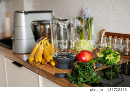 Healthy ingredients for detox smoothie drink and lifestyle diet. Glass blender bowl, apple, banana, broccoli, parsley on table top at modern home kitchen. Fresh fruits, vegetables and greens 125722838