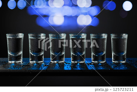 Alcoholic shots of tequila or strong drink in small wet glasses on a black table. Alcoholic shots of tequila or strong drink in small wet glasses on a black table. 125723211