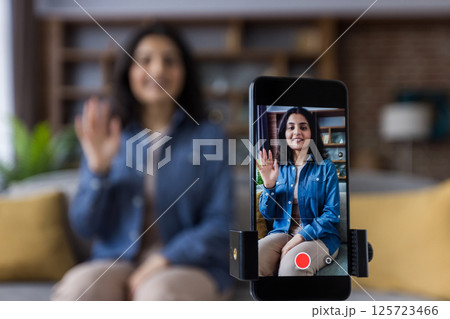 A woman records herself using her smartphone and tripod, possibly for social media, a vlog, or video call from her home. A woman records herself using her smartphone and tripod, possibly for social media, a vlog, or video call from her home. 125723466