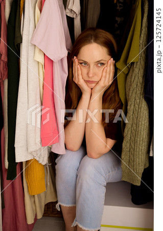Woman can't decide what to wear, closet with too many clothing. Overburdened with clothes Woman can't decide what to wear, closet with too many clothing. Overburdened with clothes 125724145