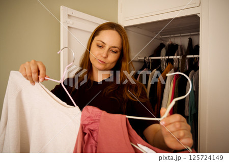 Woman choosing clothes from her closet, overwhelming amount of clothing Woman choosing clothes from her closet, overwhelming amount of clothing 125724149