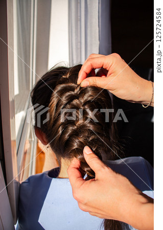 Relaxed morning routine as mom styles daughter's hair. Everyday parenting moment full of tenderness. Natural light, Direct sun light. 125724584