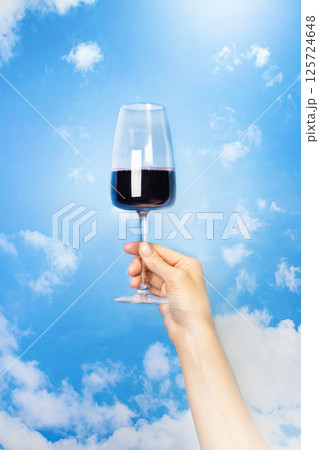 A woman's hand holds a glass of red wine against a blue sky with clouds, vertical banner A woman's hand holds a glass of red wine against a blue sky with clouds, vertical banner 125724648