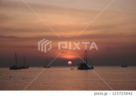 Experience a Serene Sunset Over Tranquil Waters, Adorned with Sailboats Gliding Gracefully 125725642