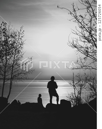 Silhouetted figures stand out against a serene landscape, evoking profound emotions Silhouetted figures stand out against a serene landscape, evoking profound emotions 125726054