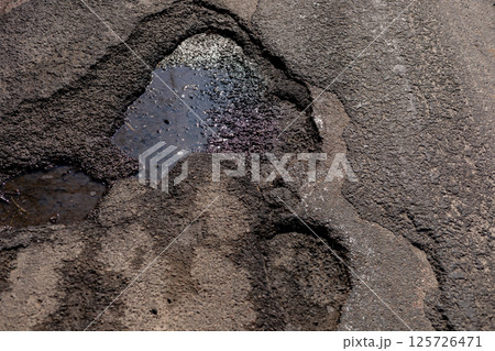 A cracked asphalt section shows a dangerous water-collecting hole, emphasizing the urgent need for traffic safety maintenance 125726471