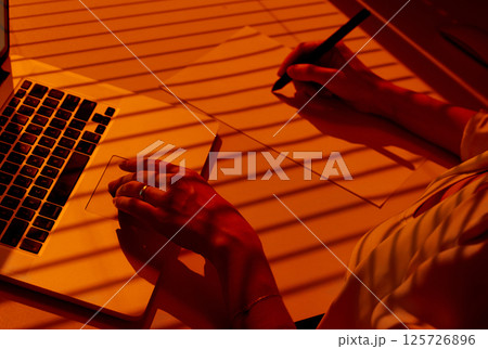 Woman Drawing with Stylus on Desk beside Laptop under Blinds. Woman Drawing with Stylus on Desk beside Laptop under Blinds. 125726896