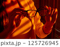 Woman Holding Eyeglasses in Golden Hour Office Light. 125726945