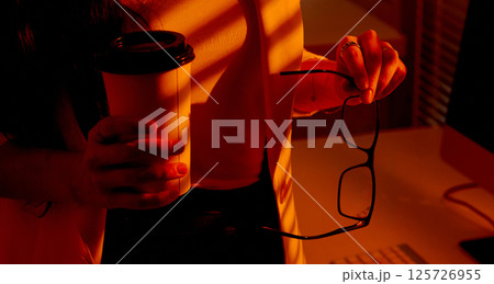 Closeup of Woman Holding Coffee Cup and Eyeglasses in Office. 125726955