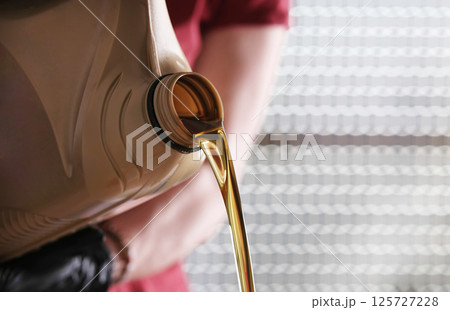 Mechanic With Canister Of Motor Oil Pouring From It 125727228