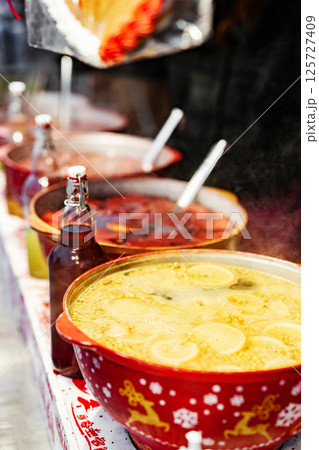 Beverages fruits and berries hot mulled wine in red pots in street food market. Colorful hot drinks at fair festival outdoors closeup Beverages fruits and berries hot mulled wine in red pots in street food market. Colorful hot drinks at fair festival outdoors closeup 125727409