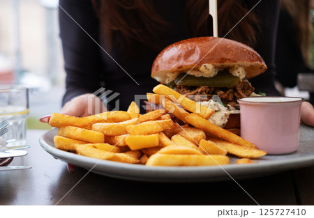 Girl Holds A Plate With Fried Potatoes And A Meat Burger In A Street Cafe Girl Holds A Plate With Fried Potatoes And A Meat Burger In A Street Cafe 125727410