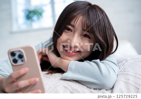 明るい窓辺でスマホを操作する若い女性が楽しげに微笑む様子 125729225
