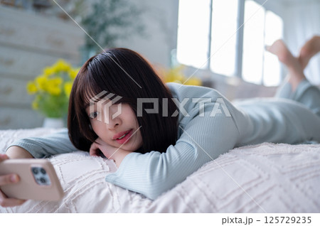 スマートフォンを見つめながら穏やかな表情を浮かべる女性のくつろぎの時間 スマートフォンを見つめながら穏やかな表情を浮かべる女性のくつろぎの時間 125729235