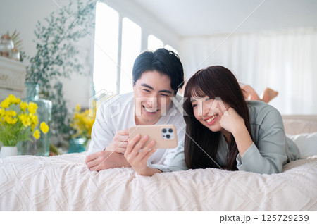 ベッドの上で仲良く並んでスマホ画面を楽しむ男女の幸せな時間 ベッドの上で仲良く並んでスマホ画面を楽しむ男女の幸せな時間 125729239