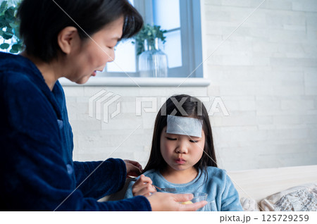 病気の娘におかゆを運ぶ母親がやさしく見守る室内の一場面 125729259