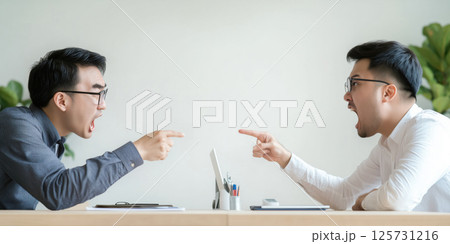Two men arguing at desk, both pointing and shouting, intense expression, modern office setting 125731216