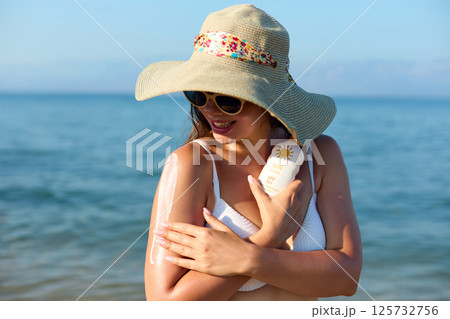 Beautiful Woman in Bikini Applying Sun Cream on Tanned Shoulder. Sun Protection. Skin and Body Care Concept. Girl Using Sunscreen. Portrait Of Female Holding Suntan Lotion or Moisturizing Sunblock. Beautiful Woman in Bikini Applying Sun Cream on Tanned Shoulder. Sun Protection. Skin and Body Care Concept. Girl Using Sunscreen. Portrait Of Female Holding Suntan Lotion or Moisturizing Sunblock. 125732756