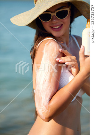 A young woman applying sun cream or sunscreen on her tanned shoulder to protect her skin from the sun. Skin and Body Care Concept A young woman applying sun cream or sunscreen on her tanned shoulder to protect her skin from the sun. Skin and Body Care Concept 125732757