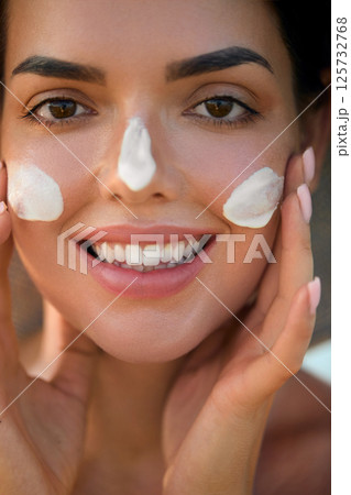 Beauty  woman with moisturising cream, sunscreen product or sun tan lotion on her cheek, luxury facial and skin care. Suntan spf and skincare cosmetics model face portrait, 125732768