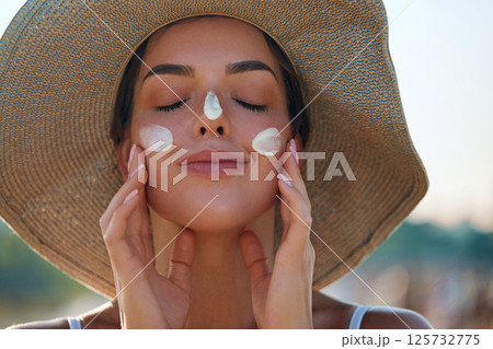 A woman smile applying sun cream on face. Skincare. Body Sun protection. Female smear sunscreen moisturizing lotion on skin. Beauty skin care concept A woman smile applying sun cream on face. Skincare. Body Sun protection. Female smear sunscreen moisturizing lotion on skin. Beauty skin care concept 125732775