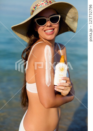 A beautiful young woman applying sun cream to her shoulder. Girl wears stylish sunglasses and enjoys the sun on a warm summer day A beautiful young woman applying sun cream to her shoulder. Girl wears stylish sunglasses and enjoys the sun on a warm summer day 125732796