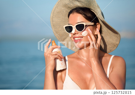 Beautiful young woman with sun cream on face. Girl holding sunscreen bottle on the beach and applying moisturizing lotion on skin.Skin care concept. Sun protection. Suntan Beautiful young woman with sun cream on face. Girl holding sunscreen bottle on the beach and applying moisturizing lotion on skin.Skin care concept. Sun protection. Suntan 125732815