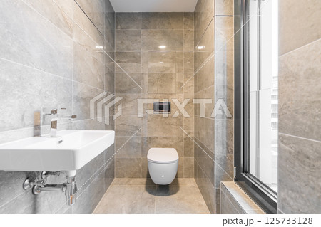 Modern bathroom with grey tiles, wall-hung toilet and tilt and turn window in contemporary apartment Modern bathroom with grey tiles, wall-hung toilet and tilt and turn window in contemporary apartment 125733128