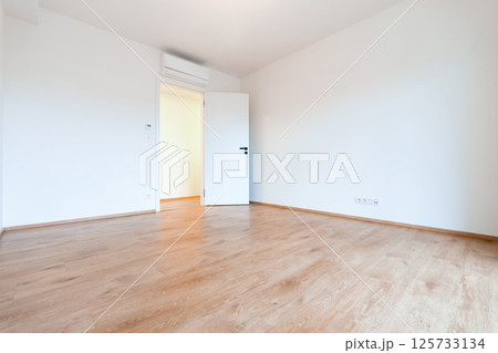 Bright and airy empty room in a contemporary apartment, featuring wooden flooring and white walls 125733134