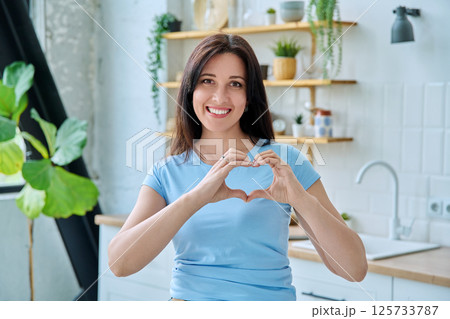 Portrait young smiling woman making heart gesture with her hands at home Portrait young smiling woman making heart gesture with her hands at home 125733787